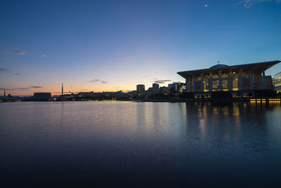 Illuminated building by lake against blue sky at dusk