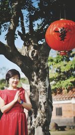 Woman with hands clasped looking at lantern hanging from tree