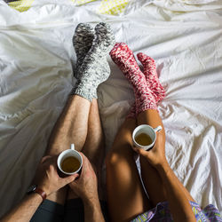 Low section of couple holding tea cup while wearing socks on bed at home