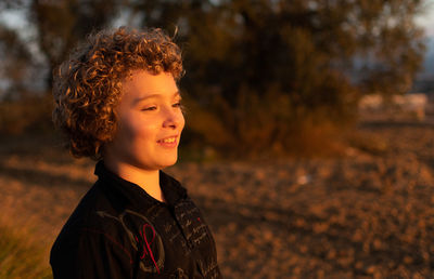 Side view of smiling boy looking away on land during sunset