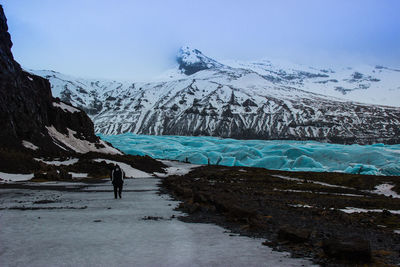 Person walking towards svinafellsjokull glaciers against sky