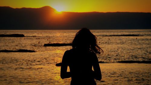 Close-up of silhouette woman against sea during sunset