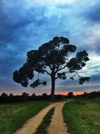 Road passing through field against cloudy sky