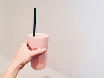 Close-up of hand holding drink against colored background