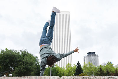 Young man gesturing shaka sign while doing handstand in city