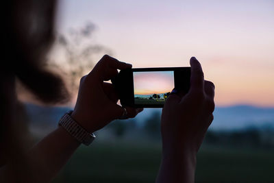 Close-up of hand photographing sunset with mobile phone 