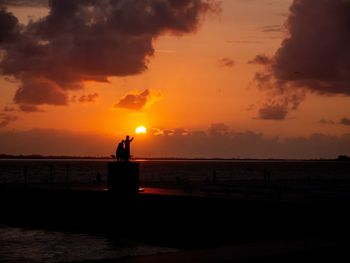 Silhouette people on beach against sky during sunset