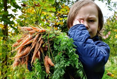 Close-up portrait of boy holding carrots at farm