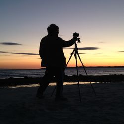 Silhouette man photographing sea against sky