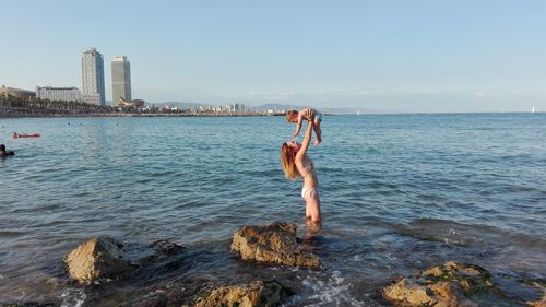 Woman and child in sea by city against sky