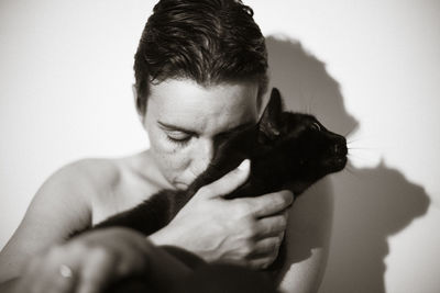 Topless woman with cat against wall