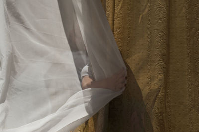 Midsection of woman standing against white curtain