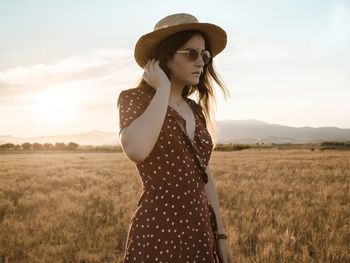Young woman wearing hat standing on field against sky
