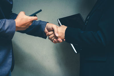 Midsection of business people shaking hands with mobile phone and book