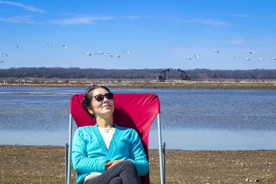 Smiling young woman sitting on beach against sky