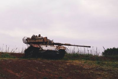 Old rusty armored tank on field against sky