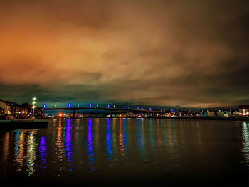 Illuminated city by river against sky at night