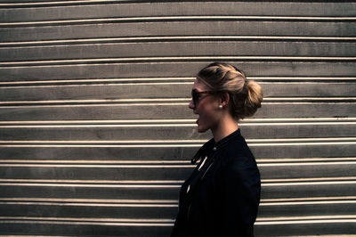 Side view of young woman with mouth open looking away by wall