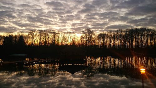 Silhouette trees by lake against sky during sunset