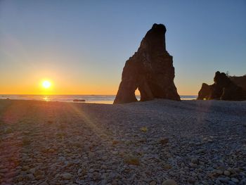 Rock formation on beach against sky during sunset