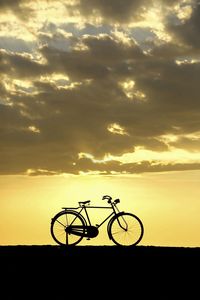 Silhouette bicycle on road against sky during sunset