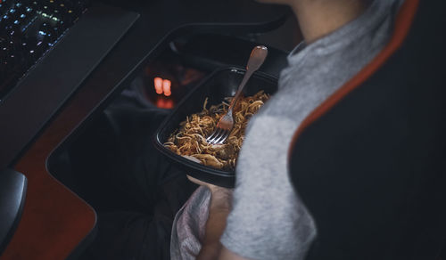 Young caucasian guy gamer holding a black container with wok food during lunch break