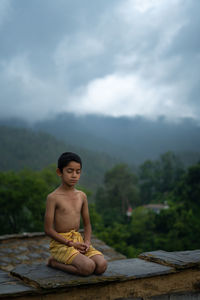 Portrait of shirtless man sitting against trees