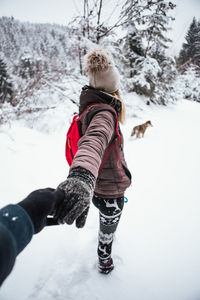 Cropped image of person holding woman hand on snow
