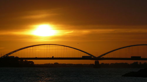 Silhouette bridge over sea against romantic sky at sunset