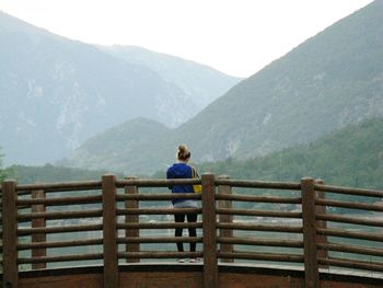 Rear view of man relaxing on railing against mountains