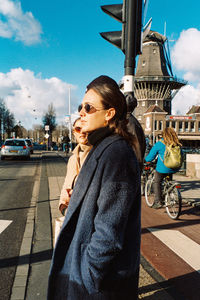Young woman looking away on street in city against sky