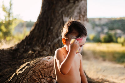 Full length of shirtless boy standing on tree trunk