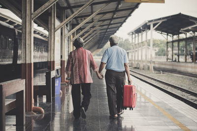 Rear view of couple holding hands while walking at railroad station platform