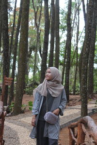 Full length of woman standing against trees in forest