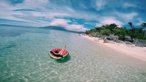 Person relaxing in inflatable ring on sea against cloudy sky