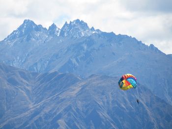 Person paragliding over mountain against sky