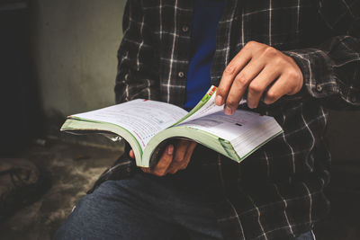 Midsection of man holding book while sitting outdoors