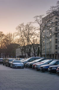 Cars parked on street by buildings against sky at sunset