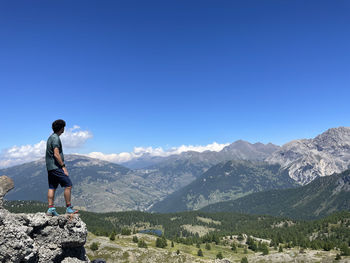 Rear view of man standing on mountain against clear blue sky