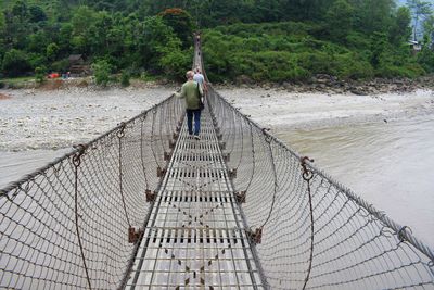 Rear view of tourists walking on footbridge over river