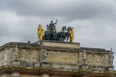 Low angle view of statues on arc de triomphe du carrousel against cloudy sky