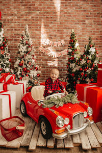 Cute boy in toy car by christmas tree