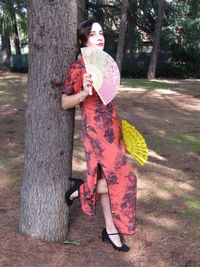 Portrait of smiling woman standing by tree trunk