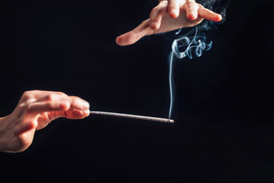 Midsection of person holding cigarette against black background