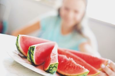 Defocused image of woman sitting in front of watermelon slices in plate on table