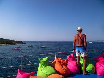 Man wearing hat against sea against clear blue sky
