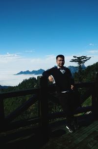 Portrait of young man sitting on railing against sky