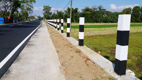 Road by fence in city against sky