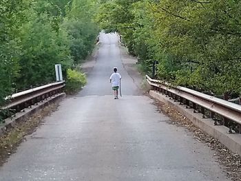 Rear view of woman walking on road amidst trees