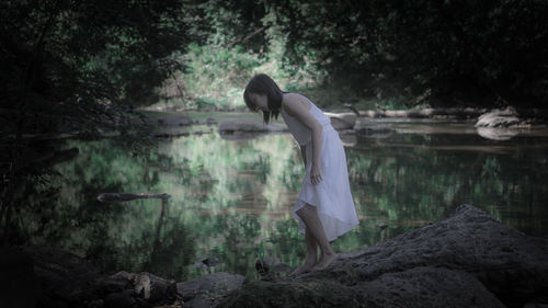 Side view of woman standing by lake in forest